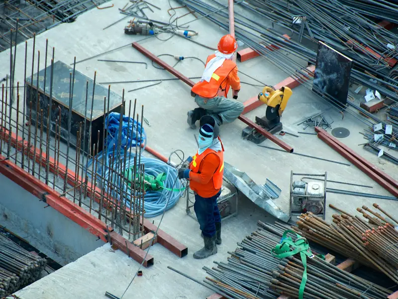 Dva stavbaři pracují na betonové desce mezi výztuží a kabely